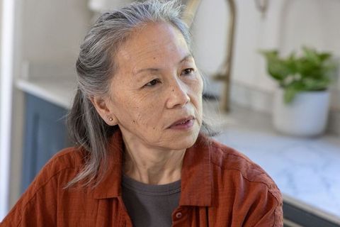 Senior asian woman sitting at kitchen counter contemplating future in soft natural light