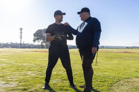 Baseball coach mentoring player on grass field during morning practice