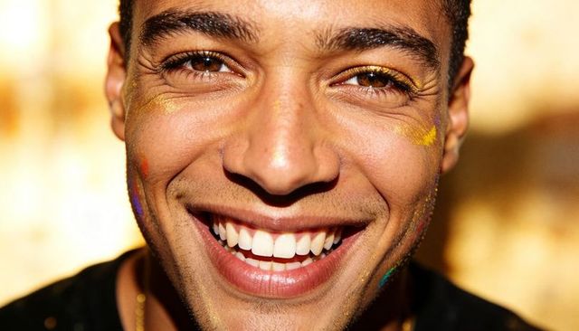Closeup smiling man showing gold glitter cheeks and colorful face paint, warm bokeh glow