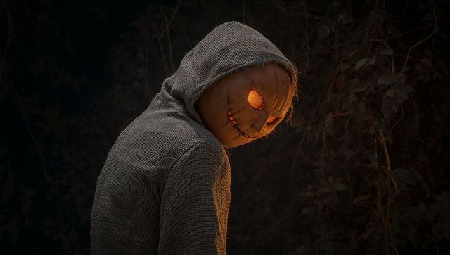 Spooky Figure with Glowing Pumpkin Head in Dark Forest