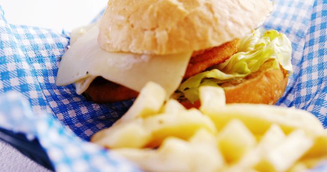 A close-up view of a chicken sandwich with cheese and lettuce, accompanied by a side of crinkle-cut fries, presented on a blue checkered napkin. The meal captures a casual, appetizing moment, ideal for a quick lunch or comfort food craving.
