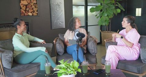 Three women recording podcast in modern lounge with microphone tablet and casual cohosts