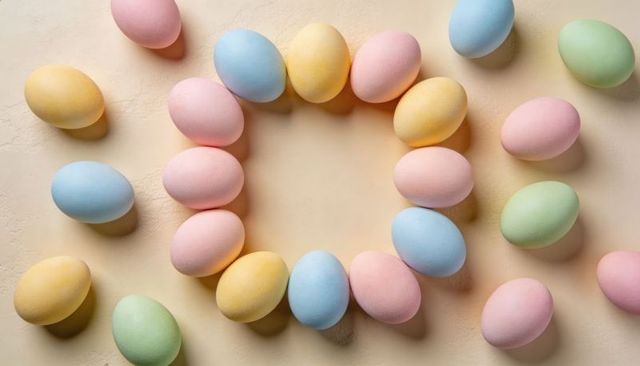 Pastel easter eggs forming hollow square wreath on cream textured surface flatlay