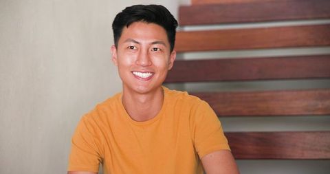 Smiling asian man in cozy foyer with modern wooden staircase