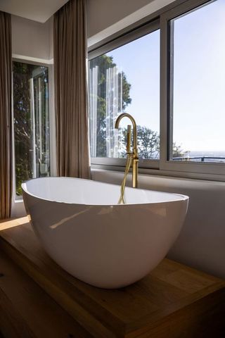 Minimalist freestanding oval bathtub on wooden platform with brass floor-mounted faucet