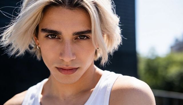 Staring platinum-blonde young man windblown hair white ribbed tank outdoor urban headshot