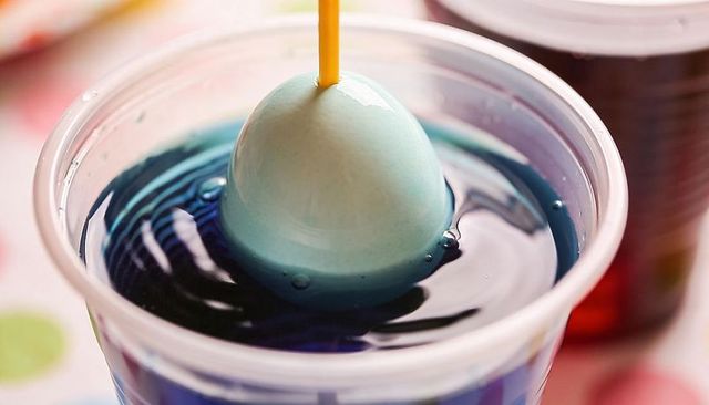 Dipping egg in blue dye using skewer for colorful easter craft closeup