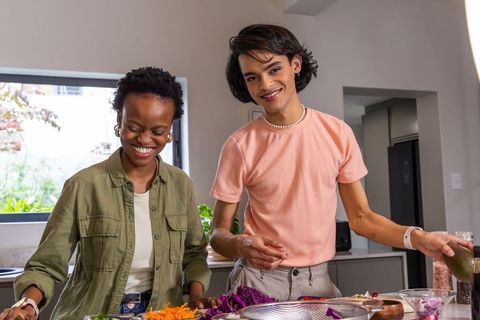 Diverse friends preparing meal, smiling and cooking together in bright modern kitchen