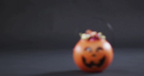 Blurred mini jack-o'-lantern candy bucket resting with autumn foliage on dark backdrop