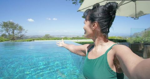Woman celebrating ocean view while standing in infinity pool at luxury resort