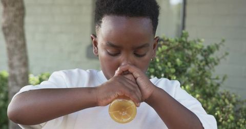 African boy sipping citrus drink from clear bottle on sunny backyard patio, close-up