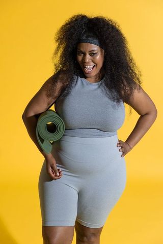 Confident african american woman in activewear holding yoga mat on yellow background