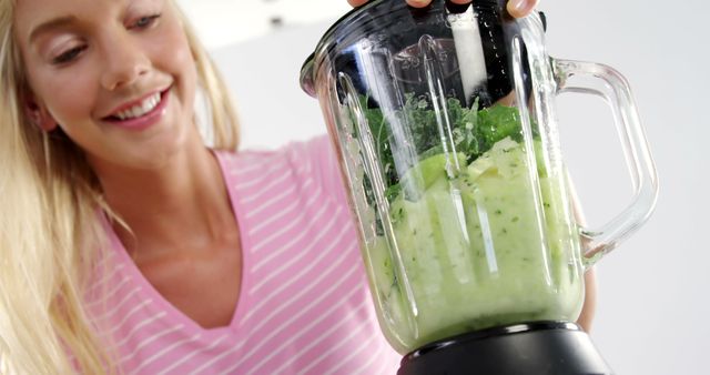 Smiling woman making green smoothie with blender - Download Free Stock Images Pikwizard.com