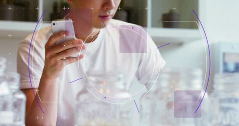 Asian man holding smartphone with futuristic hud overlay at minimalist kitchen counter