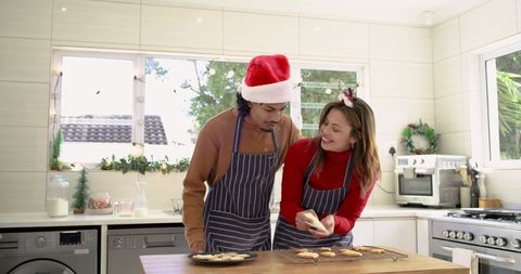 Couple baking holiday cookies in bright kitchen wearing santa hat and reindeer ears