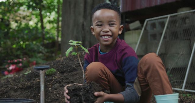 Portrait of happy african american boy holding plant in garden. Spending time outdoors, working in garden nursery.