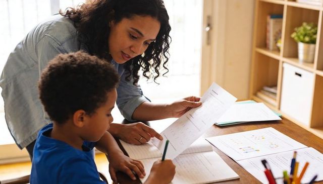 Woman tutoring child at home pointing to worksheet, homeschooling focused learning