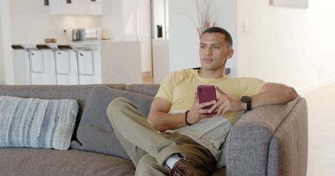Young man lounging on sofa using smartphone in modern open-plan living room