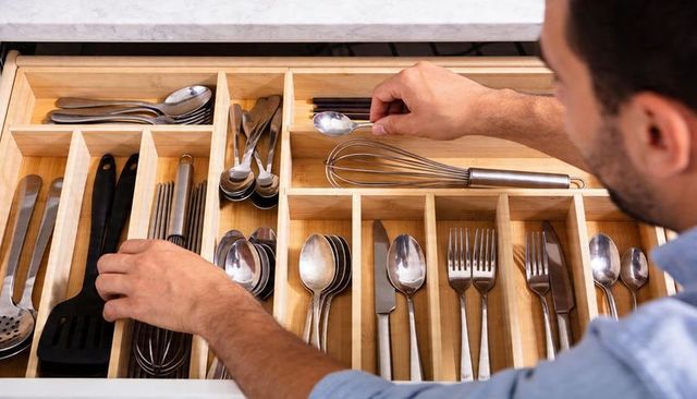Man organizing bamboo cutlery drawer with stainless utensils, whisk and spoon