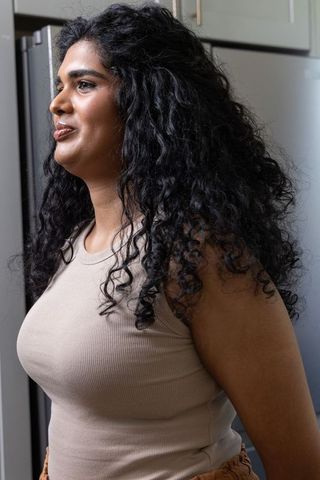 Indian woman standing in kitchen wearing beige tank and rust pants, curly hair portrait