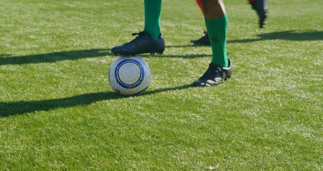 Soccer player controlling ball on green field with focus on legs and ball. Ideal for depicting sports, athleticism, soccer games, team activities, physical fitness, and competitive events.