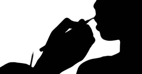 Makeup artist applying lip gloss on model silhouette