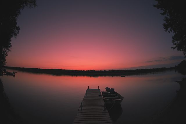 This serene scene of a sunset over a calm lake with a boat tied to a dock conveys peace and tranquility. Perfect for promoting travel destinations, outdoor activities, and relaxation retreats. Also useful as a serene background image for websites, social media, and blog posts focusing on nature and relaxation.