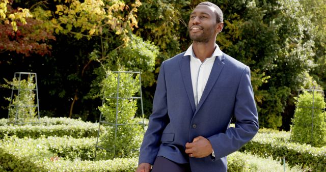 Confident man in blue suit leisurely walking in a lush garden, enjoying the sunny day and natural surroundings. Ideal for use in business promotions, lifestyle blogs, fashion advertisements, and outdoor lifestyle content.