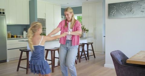 Mother and daughter spinning and laughing in bright modern kitchen for family lifestyle
