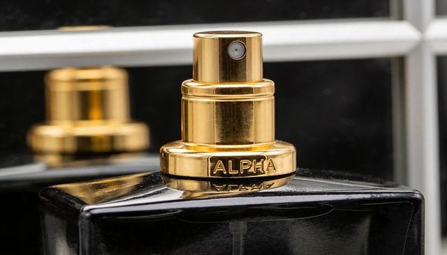 Gold-engraved alpha atomizer reflecting on mirrored vanity, luxury fragrance close-up