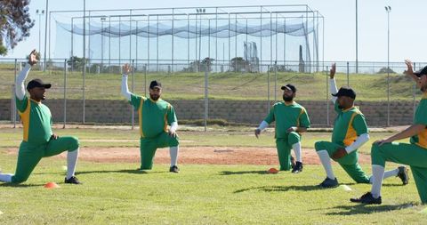 Cricket team kneeling and raising hands during warmup drill on grass field