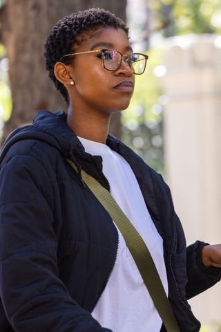 Confident african american woman wearing glasses and quilted jacket outdoors urban portrait