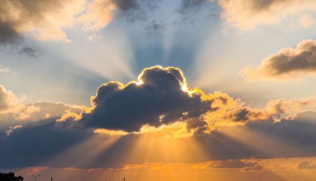 Sunset crepuscular rays breaking through dark cumulus cloud over suburban skyline
