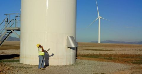 Engineer Inspecting Wind Turbine with Mobile and Laptop