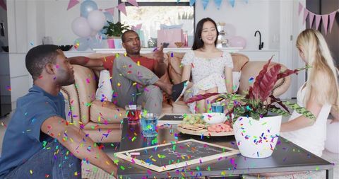 Friends celebrating in living room with confetti, balloons, snacks and casual conversation