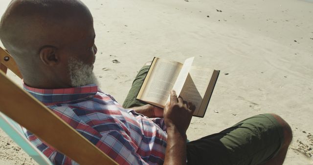 Biracial senior man sitting on a sunbed and reading a book at the beach. healthy outdoor leisure time by the sea.