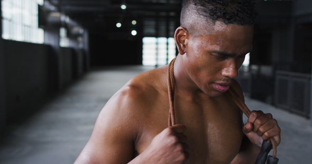 Shirtless african american man tired after skipping the rope in an empty urban building. urban fitness and healthy lifestyle.
