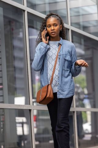 Young woman walking and talking on smartphone by glass office facade in city