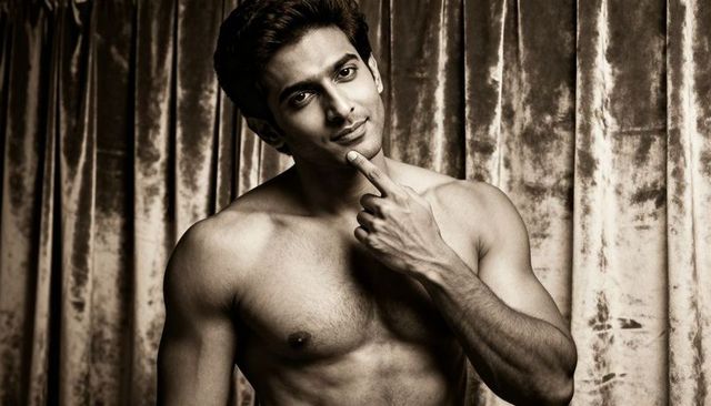 Shirtless south asian male model posing with sculpted torso against velvet sepia backdrop