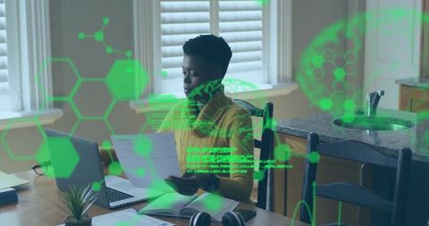 Woman reviewing documents at kitchen table with laptop and futuristic green hud