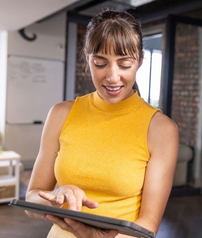 Young professional using tablet in modern coworking space wearing yellow top
