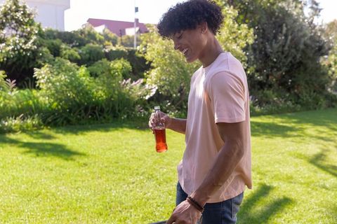 Smiling african american man holding bottle in sunny garden lawn casual lifestyle