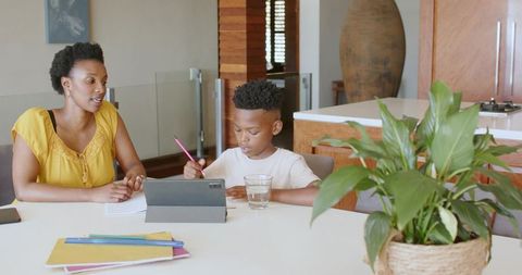 African american mother teaching son with tablet at kitchen table, homeschooling study
