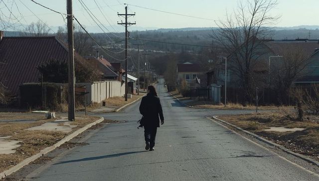 Woman walking down quiet suburban street carrying satchel under pale winter sky