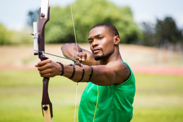 Athlete practicing archery in an outdoor field, demonstrating focus and precision. Ideal for use in sports training materials, motivational posters, or articles about archery and athletic training.