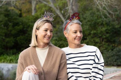 Smiling women wearing merry christmas headbands sitting outdoors in garden showing friendship