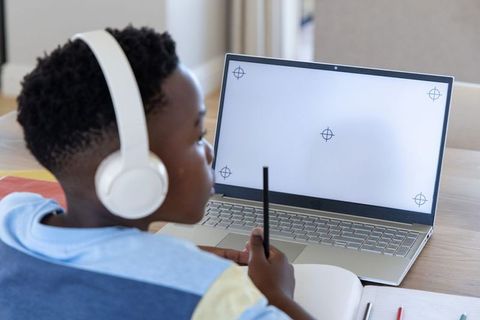 African american boy wearing headphones studying at home for remote learning with laptop