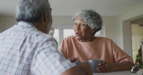 Mature couple sharing morning coffee and laughter at sunlit kitchen counter, cozy companionship