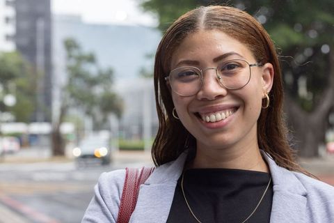 Confident african american woman smiling on city sidewalk wearing glasses and light blazer