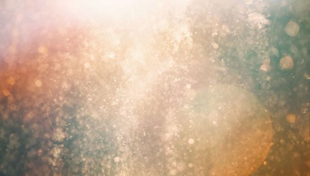 Shimmering golden-teal bokeh particles backlit glow with lens flare and dust texture